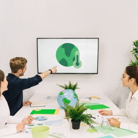 Eine Gruppe von Menschen in einem Meeting, die über den Klimawandel diskutieren, mit einem Globus und grünen Materialien auf dem Tisch.